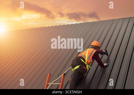 Rear view of a roofer in protective workwear installing metal sheets on a roof using a drill, Thailand Stock Photo