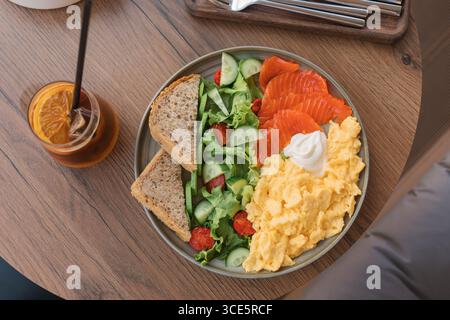 Overhead view of scrambled eggs, smoked salmon, mixed salad, multigrain bread and cream cheese on a table with an iced bumble coffee drink Stock Photo