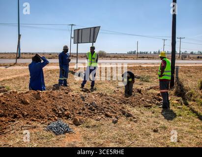 group of African workers digging a trench on the side of the highway ...