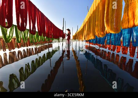 Side view of a woman standing amongst rows of colourful lotus threads hanging at Inle Lake, Myanmar Stock Photo
