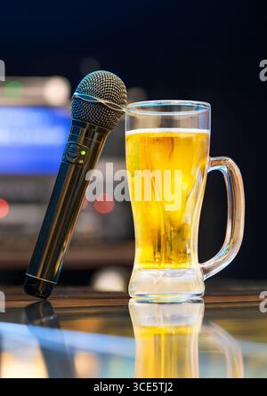 A close-up of a black karaoke microphone with green light and a glass of golden japanese beer on a glossy bar counter, evoking a lively and relaxed mo Stock Photo