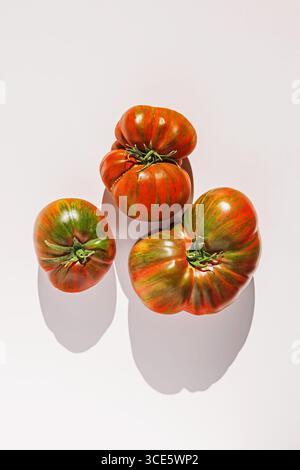 Three heirloom tomatoes with red and green stripes on a white background. Stock Photo