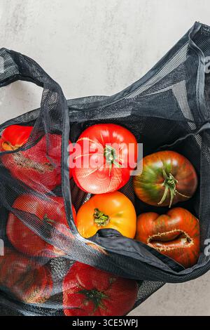 A variety of colorful tomatoes are placed inside a black reusable mesh bag. Stock Photo