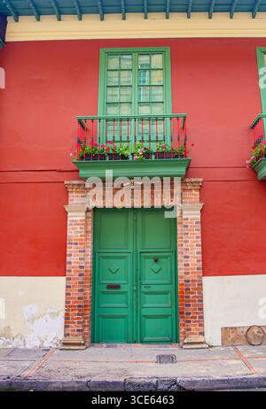 A vibrant green door framed by a red wall and lush flowers on the balcony, showcasing the charm of Bogotá, Colombia. Stock Photo