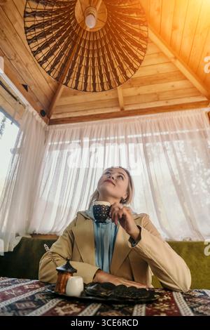 Woman Gazing Upwards While Enjoying a Drink in a Cozy Cafe Stock Photo