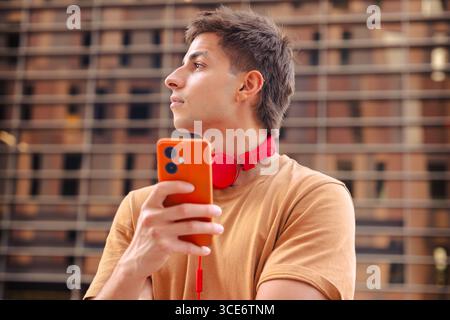 Young man with red headphones holding phone and looking away outdoors Stock Photo