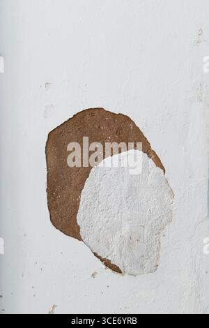 Close-up of a weathered wall painted in white, plastering has peeled off revealing unpainted wall. Abstract high resolution full frame textured backgr Stock Photo