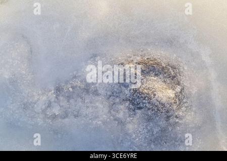 Close-up of bubbles and a stone under ice on a frozen lake in the winter, viewed from above. Abstract full frame textured background. Copy space. Stock Photo