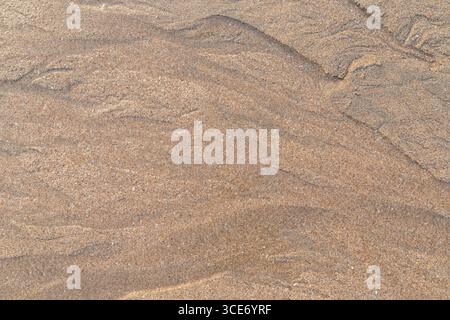 Abstract shapes & patterns in grainy sand and flowing water on the beach on a sunny day, viewed from above. Abstract textured natural sandy background Stock Photo