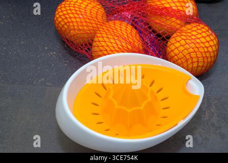 Orange juicer with fresh oranges in a net bag on a dark kitchen table surface Stock Photo