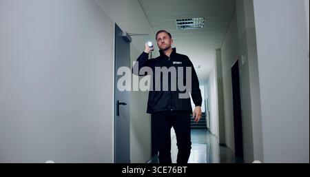 Night Warehouse Security Guard Patrols In Uniform With Flashlight For Safety. Possible Professions: Security Guard Stock Photo
