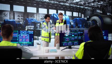 Diverse Team Of Engineers Operating Modern Turbine At Power Plant. Stock Photo
