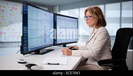 Senior Woman Audits Financial Data On Computer Screen In Office. Stock Photo