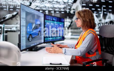 Senior Engineer Monitoring Electric Car Assembly Line With Female Technician Stock Photo