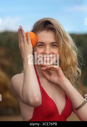 Portrait of beautiful blonde woman with juicy tasty orange on summer nature background Stock Photo