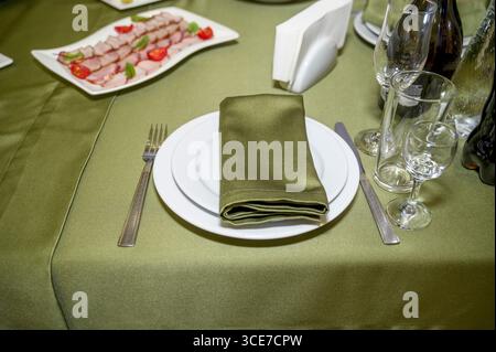 festive table in the restaurant hall, bright with green tablecloth and napkin. Table setting in the restaurant. Table setting for brunch with a variet Stock Photo