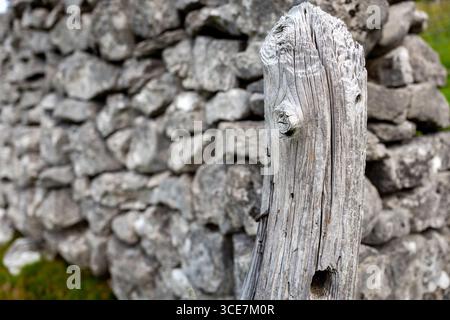 Grey decaying wooden gate post with a grey Dry Stone wall made of Limestone. Stock Photo