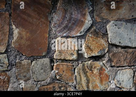 A detailed view of a stone wall, showcasing diverse textures, colors, and shapes within the rocks, emphasizing a rustic and natural architectural Stock Photo