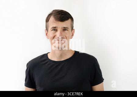 Smiling man in a black t-shirt standing casually against a white background, exuding confidence and positivity. Happy middle-aged man resting Stock Photo