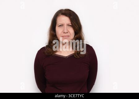 A serious woman wearing a maroon top is standing against a white gradient background. Her expression conveys determination, thoughtfulness Stock Photo