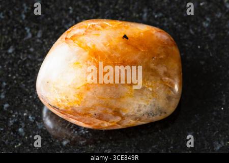 sample of tumbled orange quartz mineral on black granite background close up from South Urals, Russia Stock Photo