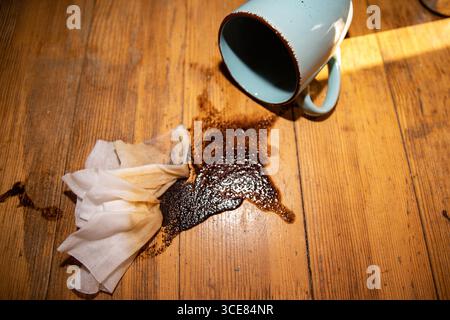 Overturned ceramic cup with spilled coffee on wooden table Dirty stain with napkins symbol of accident mess and cleaning problem Stock Photo