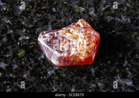 sample of raw hyacinth zircon crystal on black granite background close up from Tanzania Stock Photo