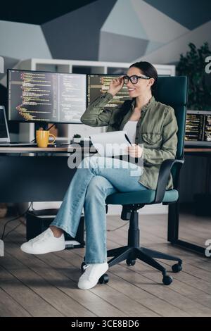Charming female IT specialist working on programming in a modern office setting, smiling confidently Stock Photo