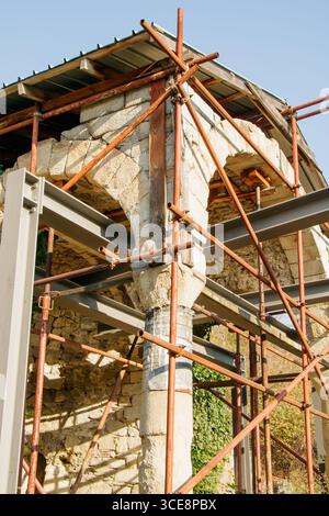 Workers are renovating a historical stone building using scaffolding and structural support to secure its integrity. The clear sky enhances the focus Stock Photo