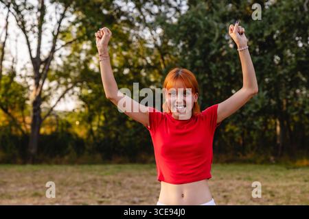Young woman celebrating with raised arms in a park Stock Photo