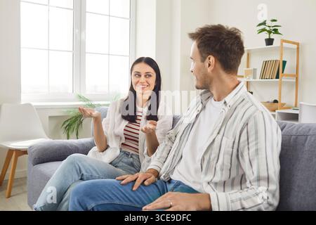 Smiling young couple on sofa in living room having friendly conversation and enjoying quality time. Stock Photo