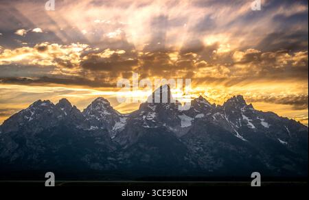 Sun Rays Burst Through Evening Clouds Behind The Grand Teton Range in early Summer Stock Photo