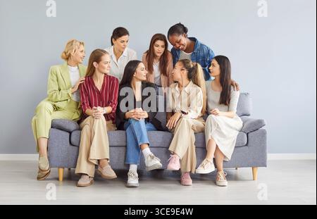 Young diverse women group coworkers sitting on sofa on gray background and talking Stock Photo