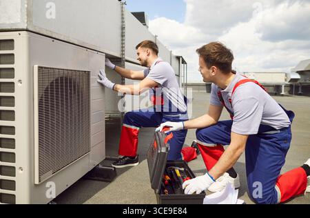 Team Of Engineers And Electricians Repairing Air Conditioning System On Roof Stock Photo