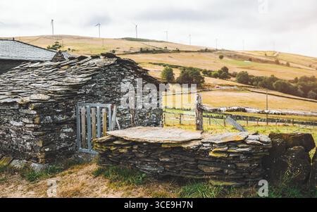 Traditional Asturian rural architecture with rustic stone house built from slate and local rock masonry, wooden gate and fence, set in countryside hil Stock Photo