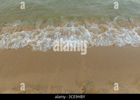 Small sea waves breaking on sandy beach in soft sunset light Stock Photo