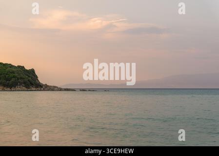 Pastel-colored sunset sky over calm sea and distant coastline Stock Photo