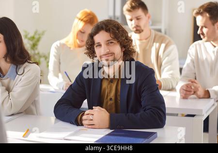 Portrait of smiling university student sitting at desk in classroom during educational lecture. Stock Photo