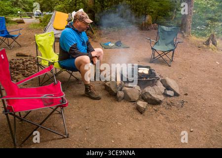 Man sitting on folding camp chair in the Riverside Campground watching camp fire, Willamette National Forest, Linn County, Oregon, USA Stock Photo