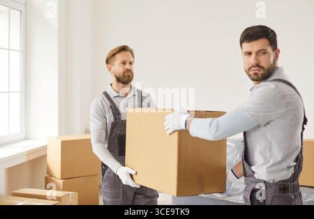 Two movers carrying cardboard boxes from clients house, unload items, dressed in overalls Stock Photo