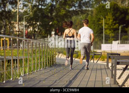 Back view of young sporty couple wearing sportswear running together in the park. Stock Photo