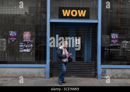 Glasgow, UK, 16th August 2025. Woman checks her phone in front of closed and disused shop premises, with sign reading ÔWowÕ, in the streets of Glasgow, Scotland, 16 August 2025. Stock Photo