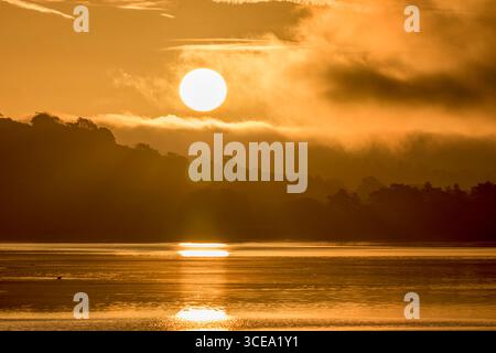 Sun rising over Blagdon Lake, Somerset uk with sunrays and reflection in lake Stock Photo