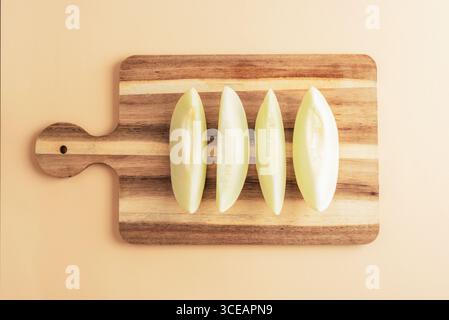 Four Piel de sapo melon slices on wooden cutting board on beige background. Top view, flat lay. Stock Photo