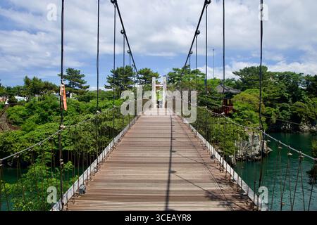 A straight‑on view along the wooden Yongyeon Cloud Bridge shows its suspension cables and deck leading over green water toward the opposite towers in Stock Photo