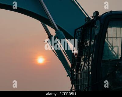 Excavator arm and cabin silhouette against a warm sunset sky, symbolizing construction and industry. Stock Photo