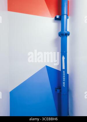 Blue industrial air freshener pipe against a geometric red, white, and blue wall design in a modern interior Stock Photo
