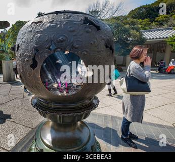 Incense burning in metal stand, woman praying at base of the Great Buddha of Kamakura a monumental outdoor bronze statue of Amitābha Buddha, Kōtoku-in Stock Photo