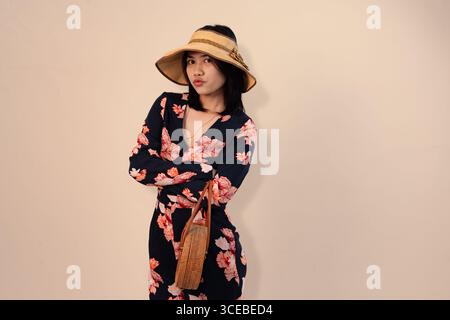 fashionable woman posing in floral dress with straw hat and handbag Stock Photo