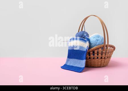 Blue and white knitting balls in basket with knitting needles and knitted scarf on pink background. Set for the hobby of knitting warm clothes or toys. Concept needlework Stock Photo